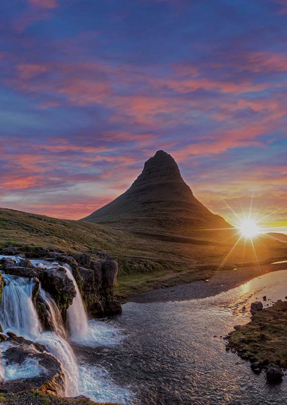 A waterfall descending into a river; a tall conical mountain in the distance.