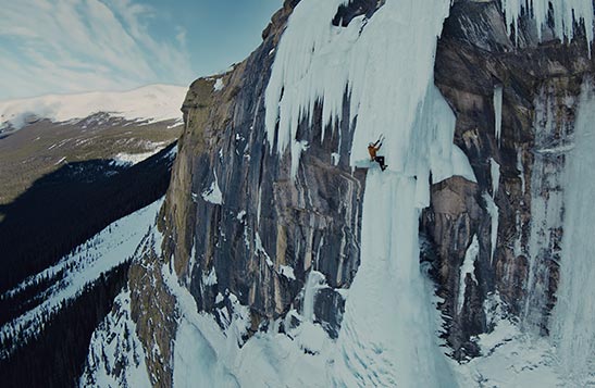 An ice climber ascends a frozen waterfall high up in the mountains.