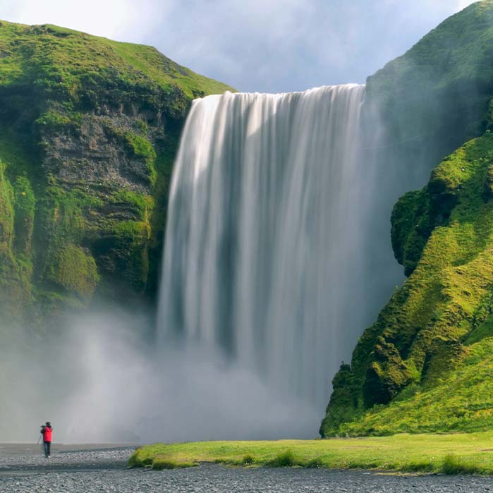 A tall waterfall descends between grassy cliffs.